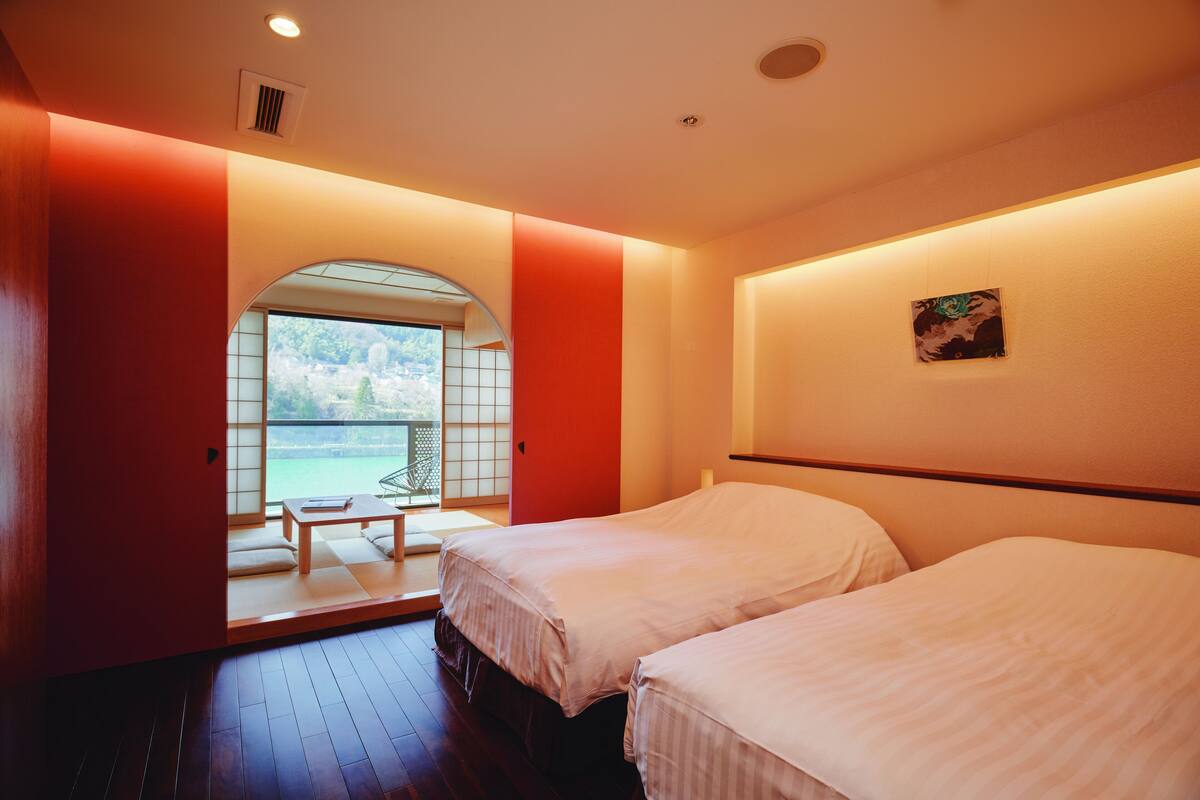 A hotel room with two beds, a view of a balcony, and a small table with a chair.
