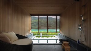 A modern bathroom with a large window, a wicker chair, a wooden stool, and a shower area. - River Retreat GARAKU (Toyama)