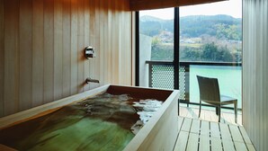 A modern bathroom with a wooden interior, a bathtub, and a view of a body of water and mountains through a large window. - River Retreat GARAKU (Toyama)