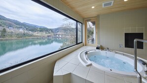 A spa room with a large window overlooking a lake and hills, a hot tub, and wooden ceiling. - River Retreat GARAKU (Toyama)