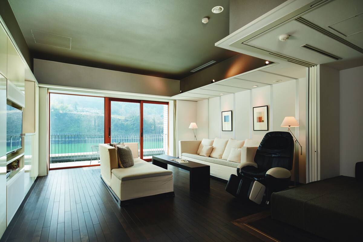 A modern hotel room with a balcony, a sofa, a chair, a coffee table, and a bed.