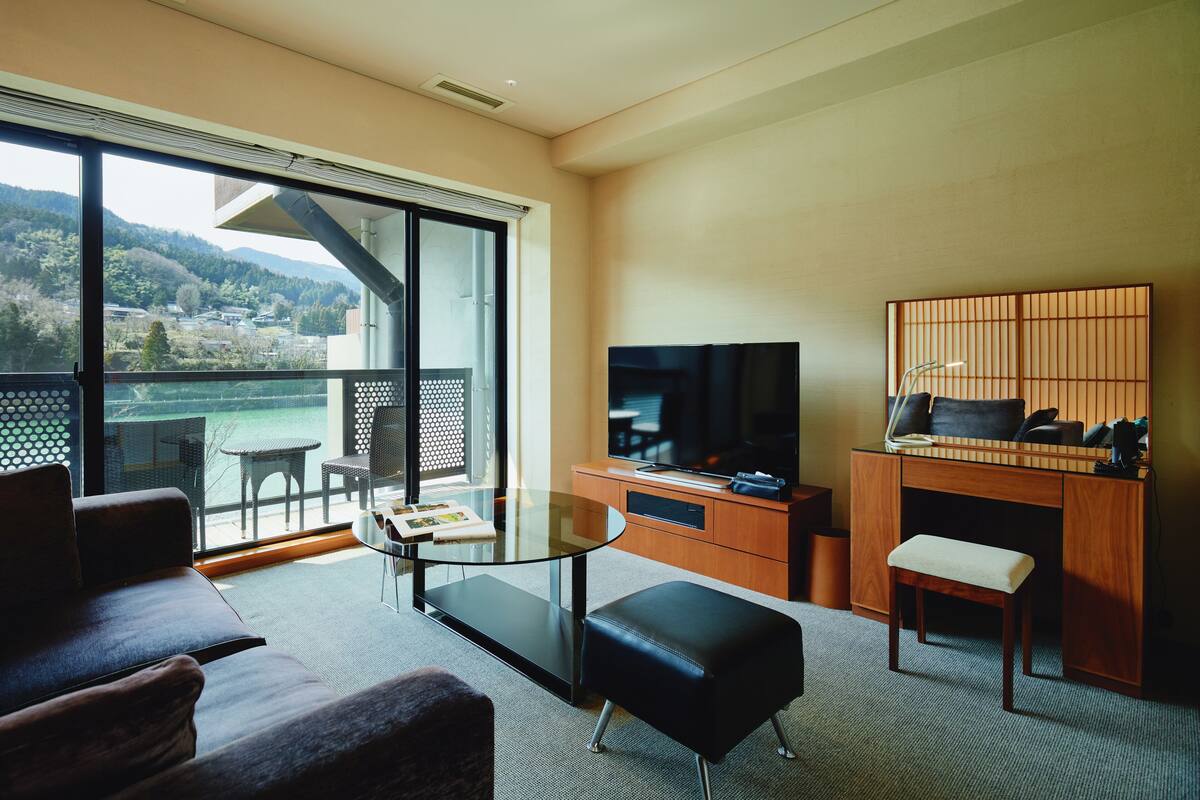 A modern living room with a glass table, a sofa, a TV, and a desk with a computer.