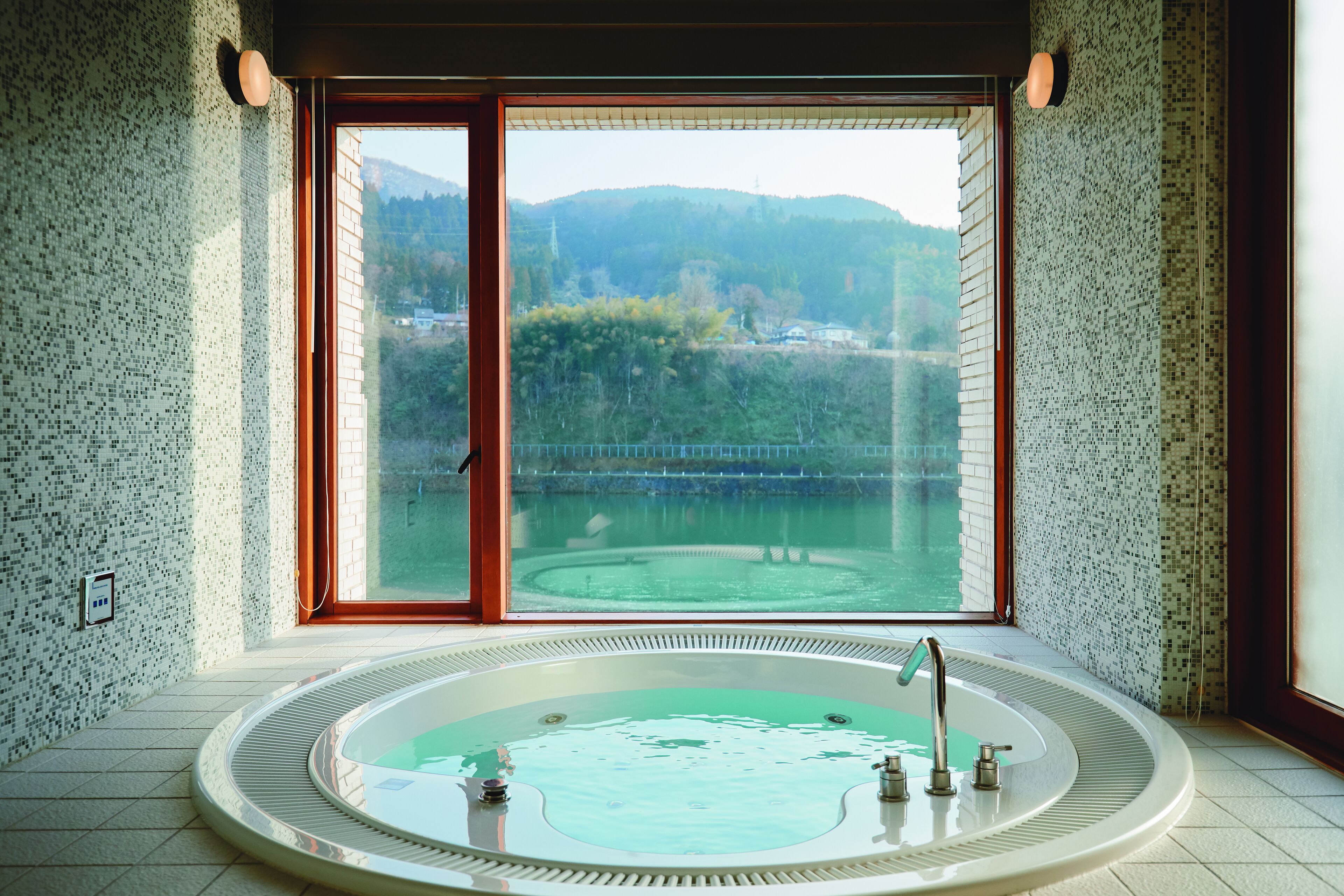 A spa room with a large bathtub, a view of a lake, and a tiled wall.