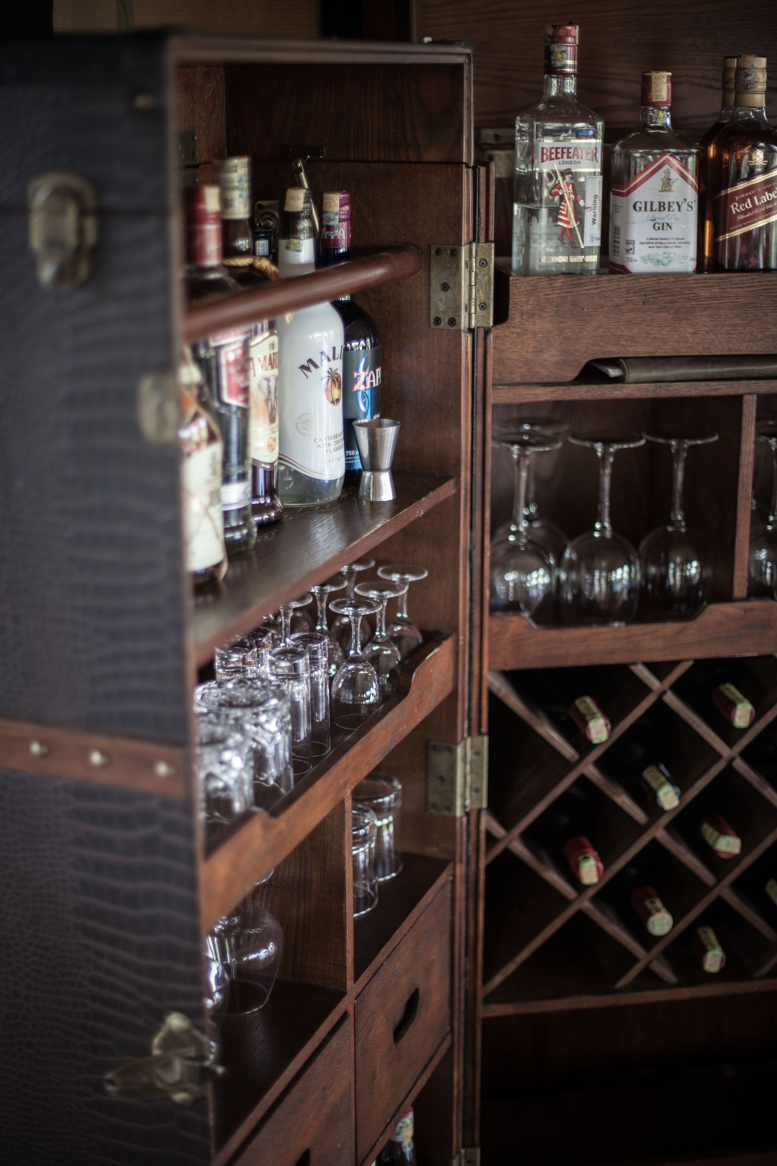 A wooden cabinet with shelves holding various liquor bottles and wine glasses.