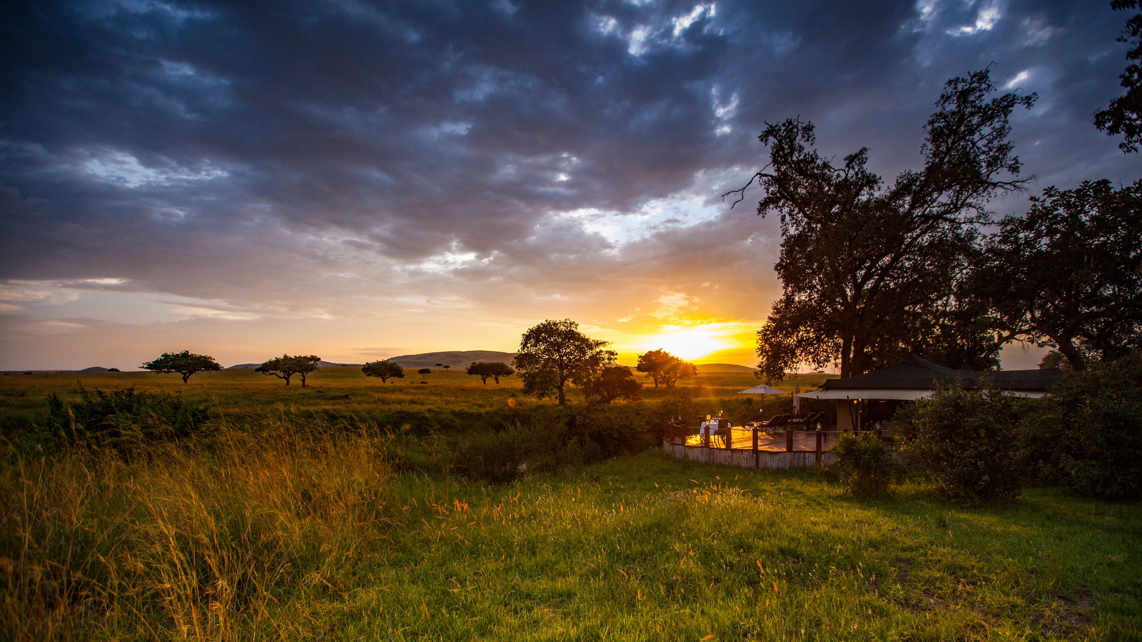 A serene landscape with a sunset, a grassy field, and a small outdoor seating area with tables and chairs.