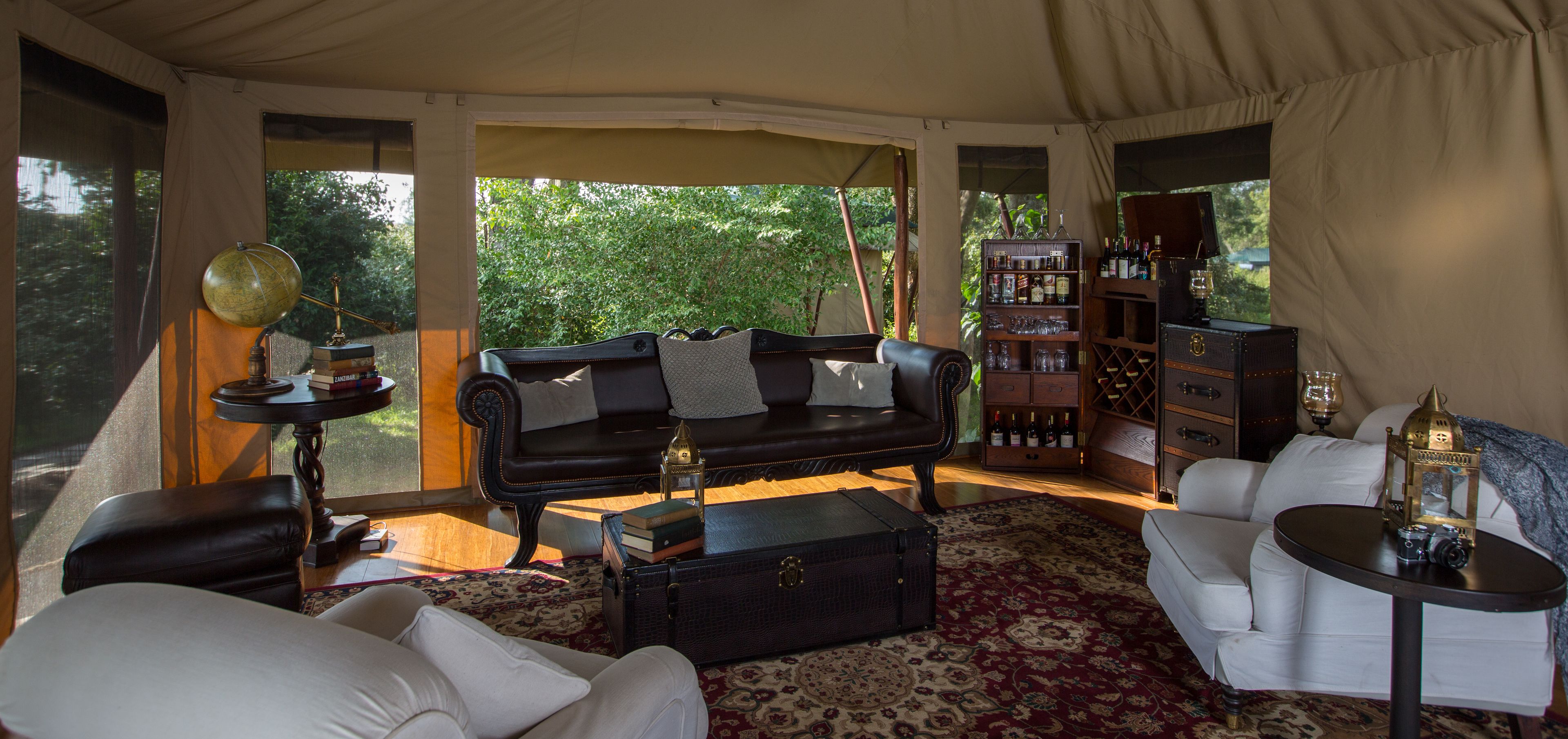 A tented room with a leather sofa, a white armchair, a small table, a globe lamp, a bookshelf, and a suitcase.