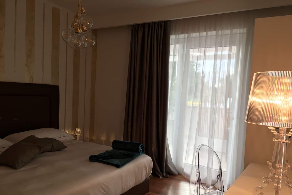 Une chambre d’hôtel avec un lit, une chaise, une lampe et une fenêtre avec des rideaux.