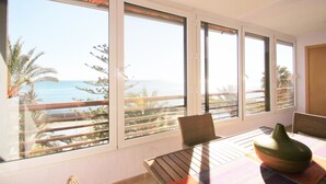 A room with a view of the sea, a table with chairs, and a vase on the table.