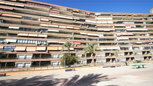 A multi-story building with balconies, air conditioning units, and a paved area with a bench.