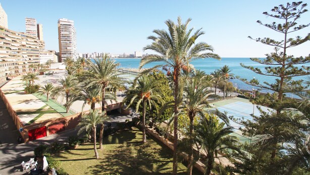 A coastal resort with palm trees, a tennis court, and a view of the sea.