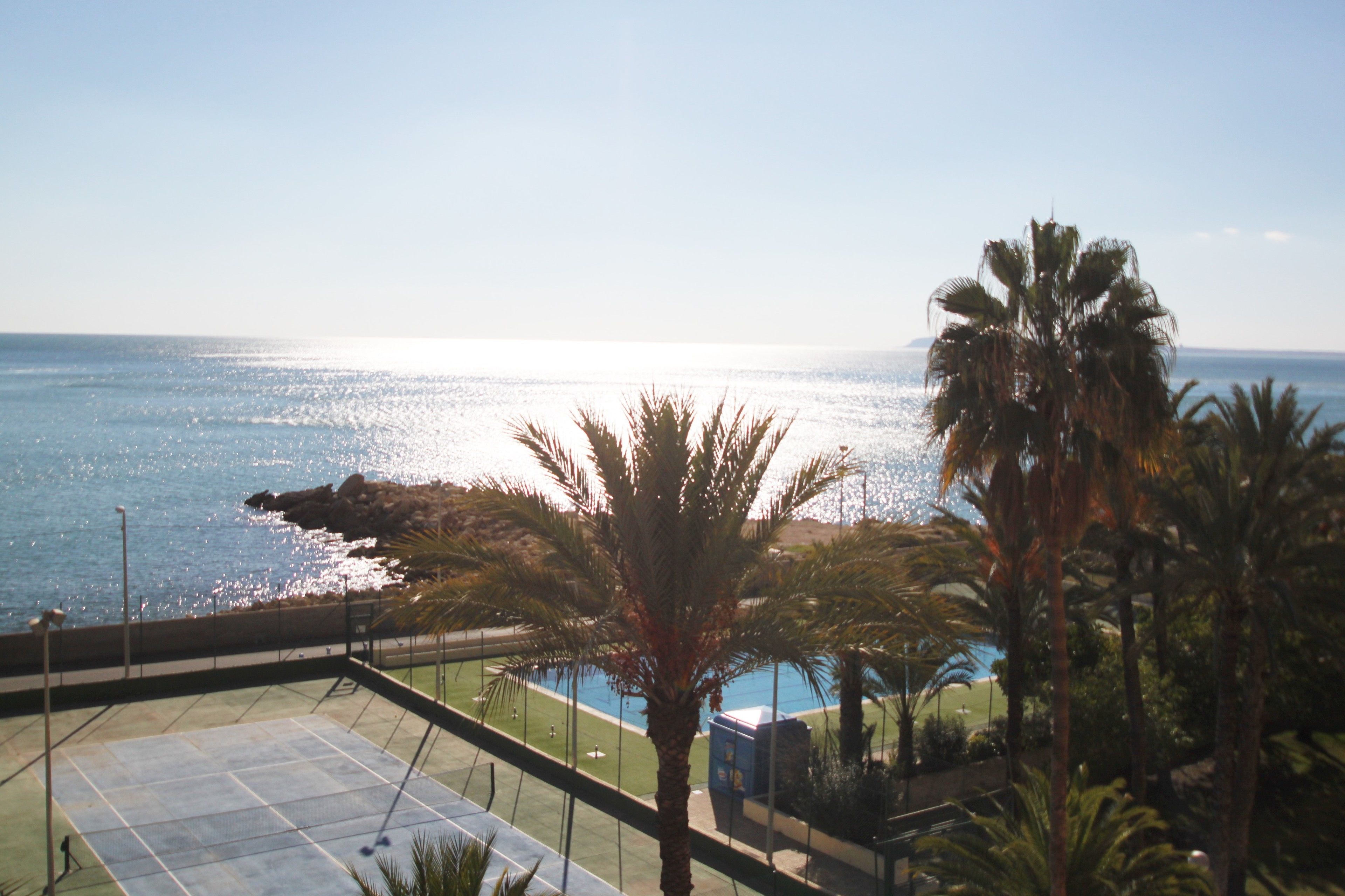A view of a pool area with a clear view of the ocean and a rocky shoreline.