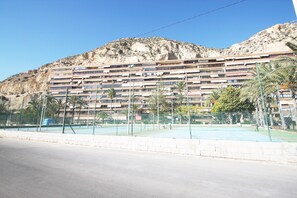 A multi-story hotel with balconies, a swimming pool, and a mountainous backdrop.
