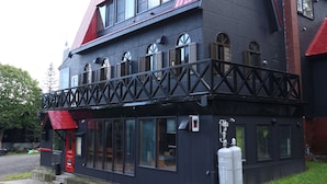 Un immeuble de deux étages avec une façade noire, un toit rouge et un balcon doté d’une balustrade noire.