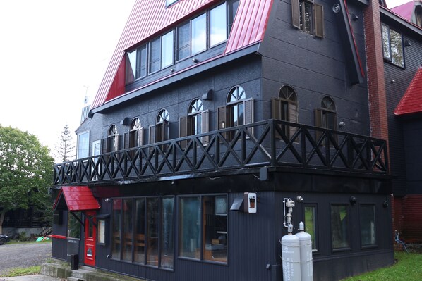 A two-story building with a black facade, red roof, and a balcony with a black railing.
