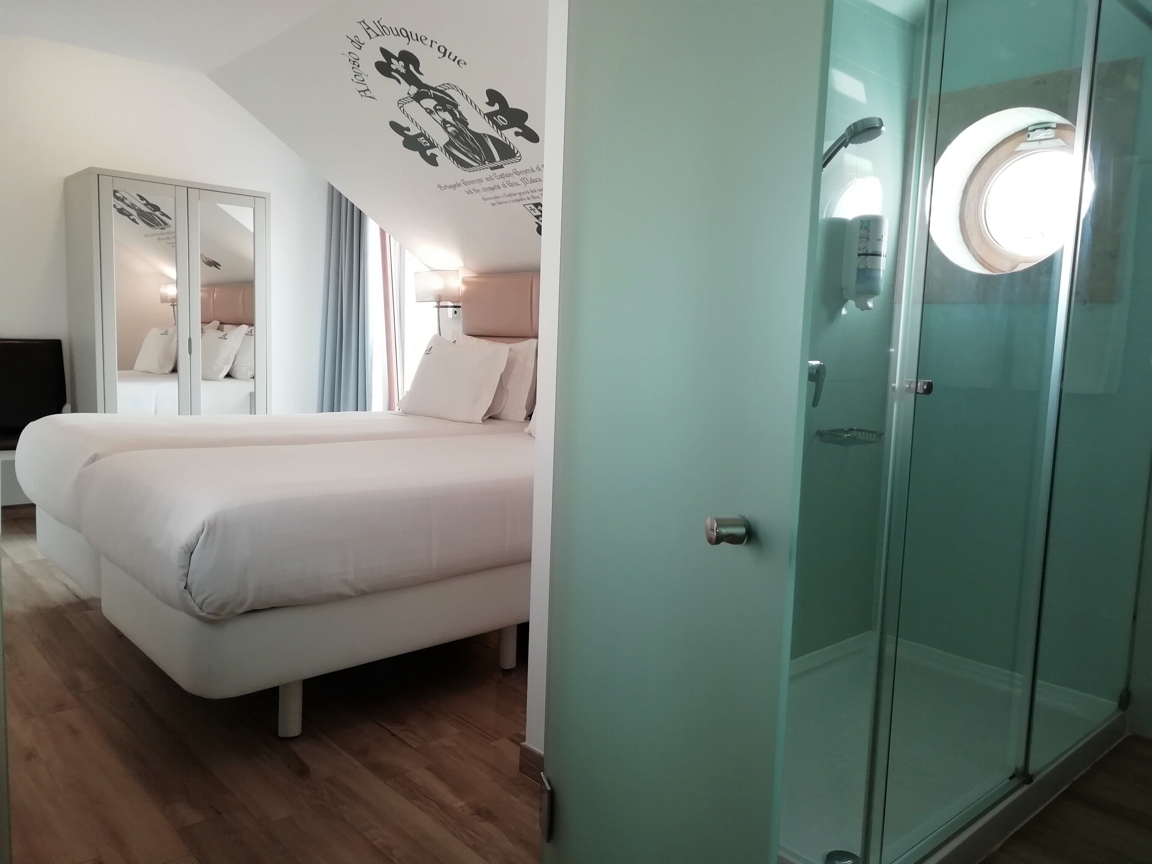 A hotel room with a bed, a wardrobe, and a glass shower enclosure.