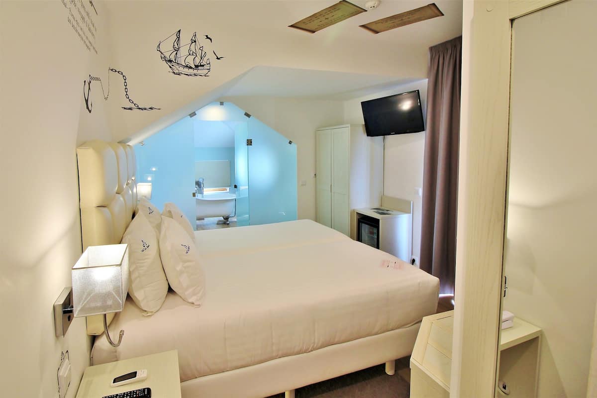 Une chambre d’hôtel avec un lit, une télévision, un bureau et une salle de bain visible à travers une porte ouverte.