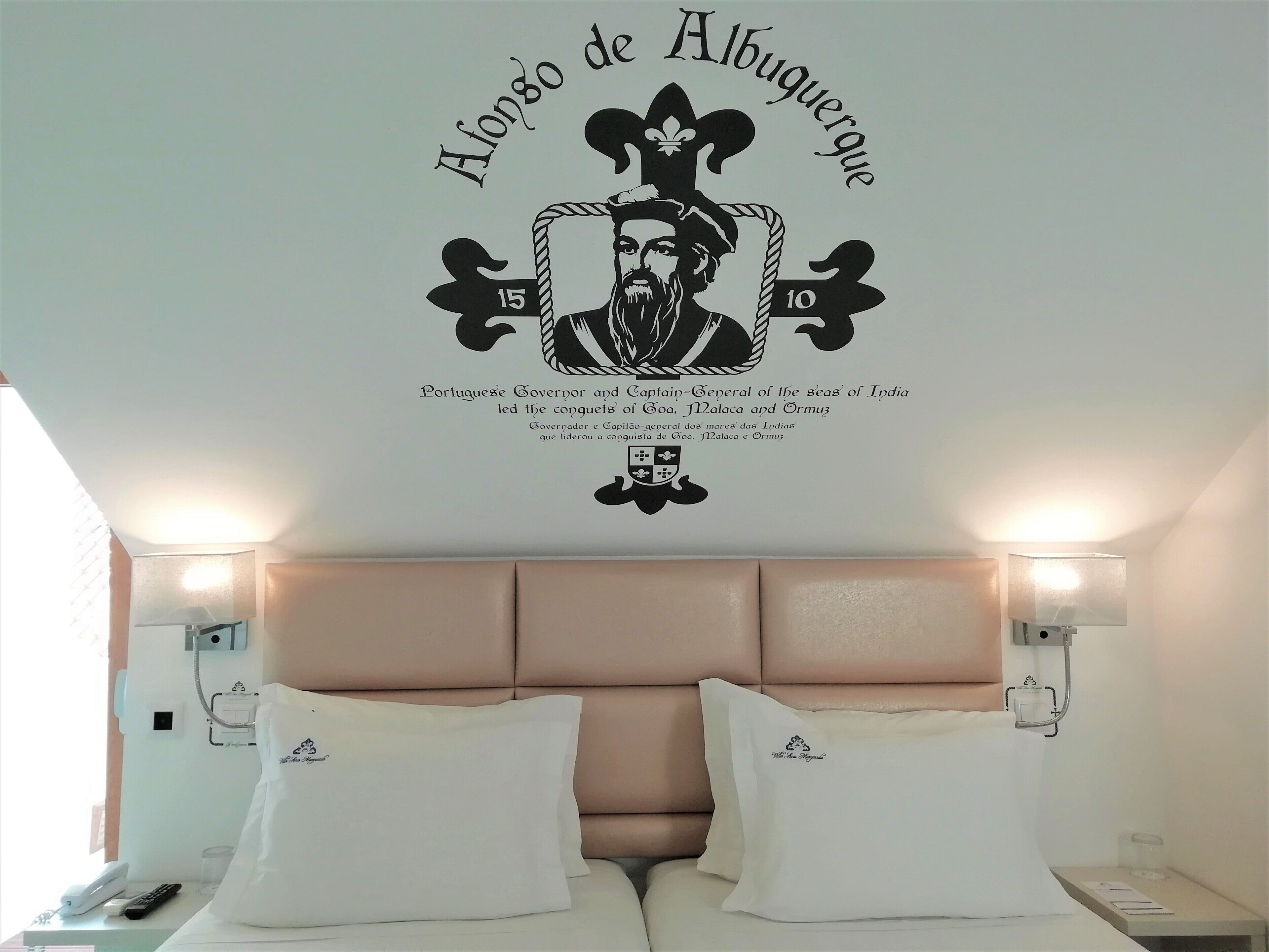 A hotel room with a large emblem on the wall, a bed with white linens, and bedside lamps.