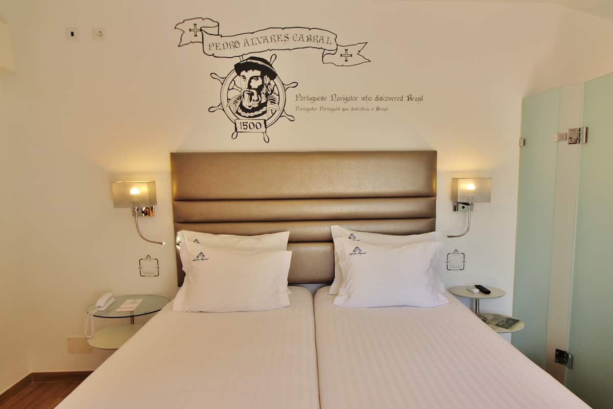 Une chambre d’hôtel avec un grand lit, deux tables de chevet et des lampes fixées au mur.