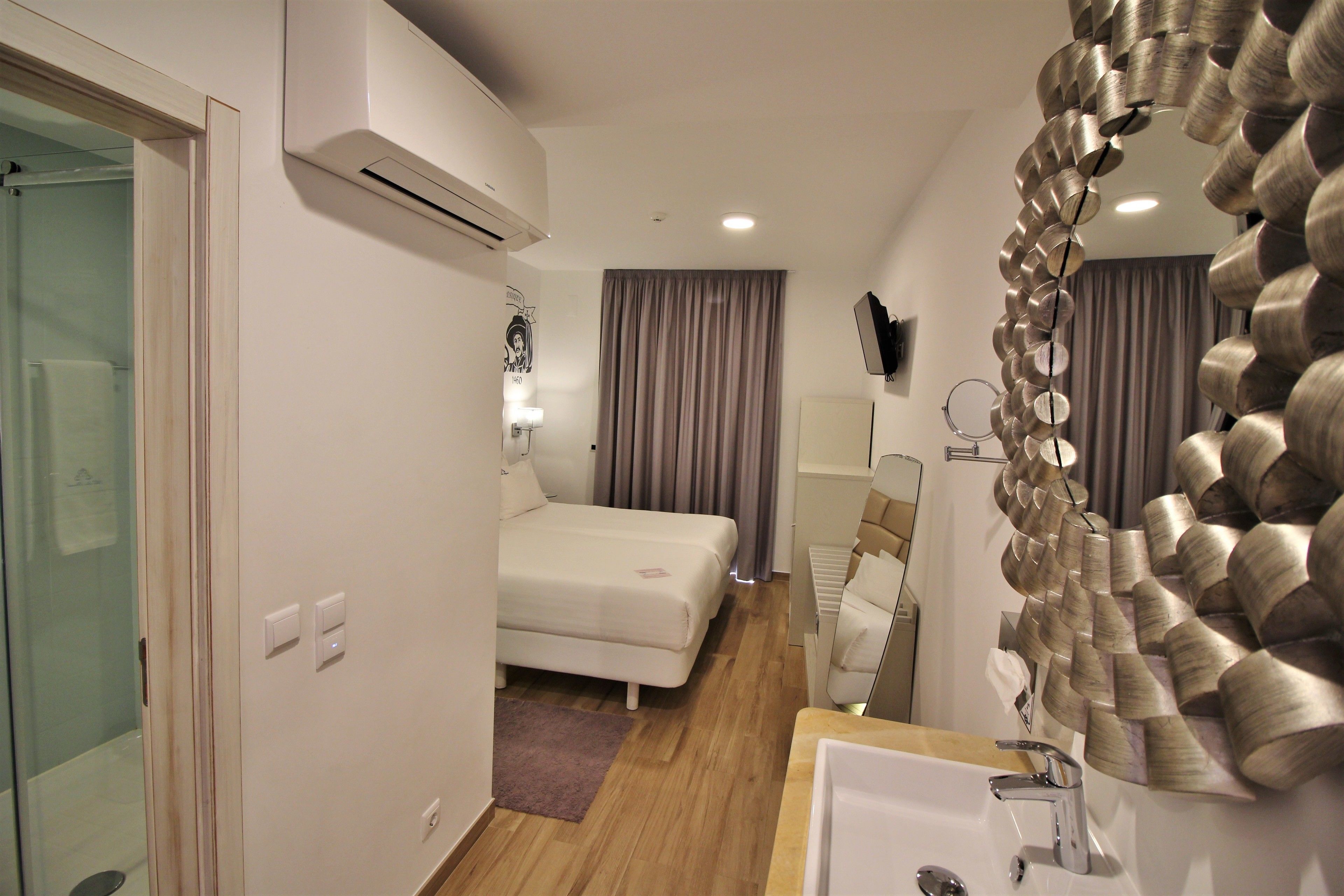 A hotel room with a bed, a bathroom with a sink and mirror, and a shower area.