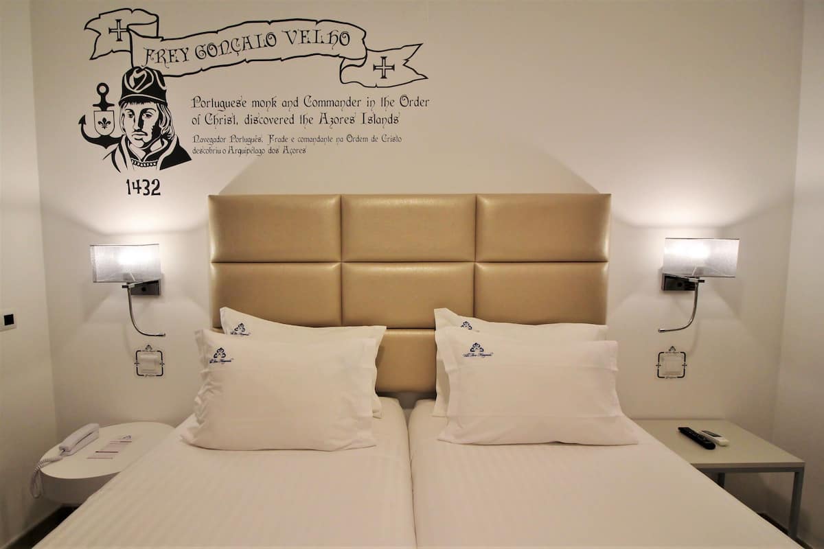 Une chambre d’hôtel avec un grand lit, deux tables de chevet, une lampe fixée au mur et un élément décoratif mural.