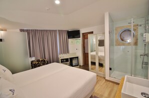 Ein Hotelzimmer mit Bett, Schreibtisch, einem kleinen Tisch, einer Duschkabine und einem Glaskasten-Badezimmer.