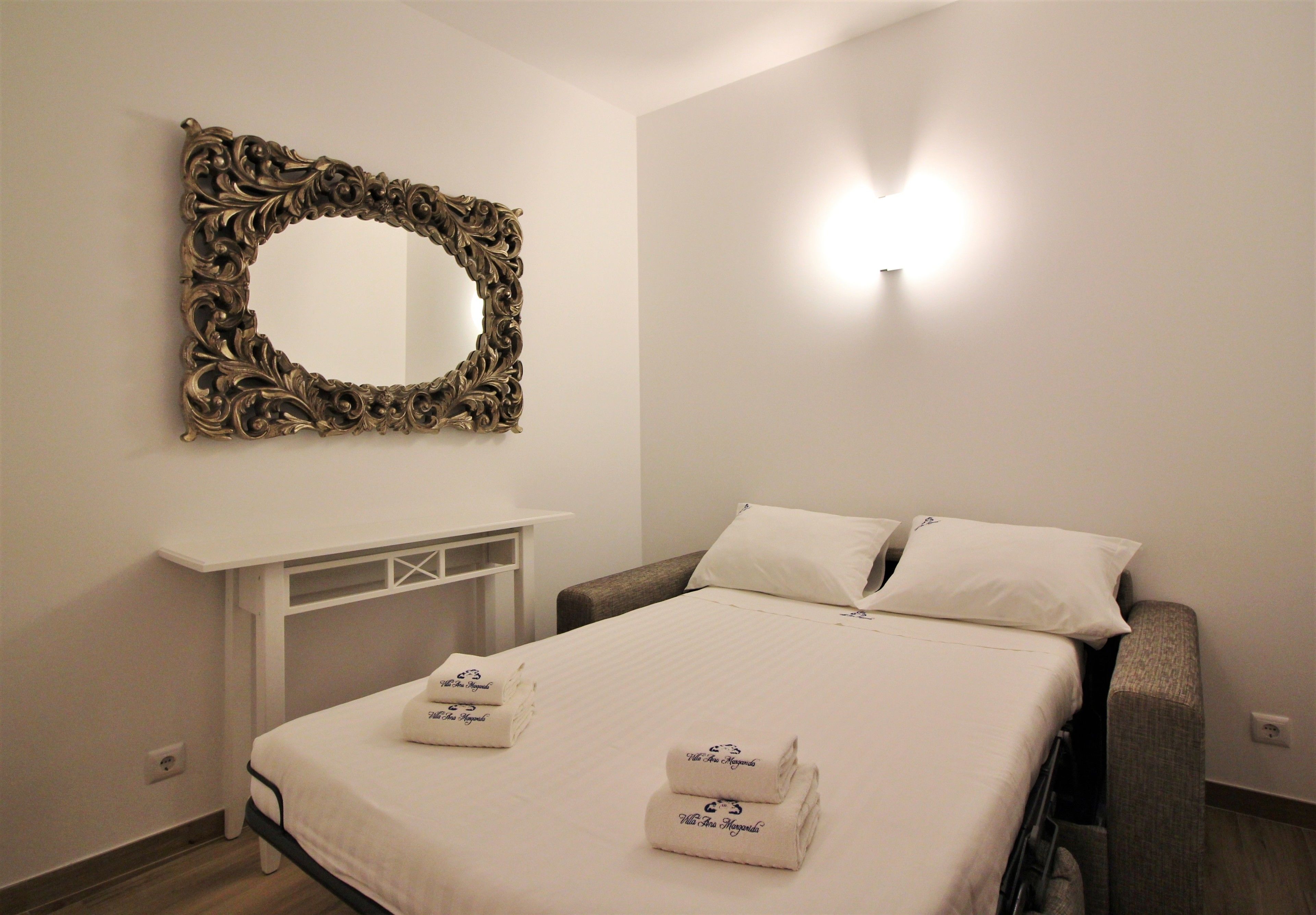 Una habitación de hotel con un espejo grande y ornamentado, una cama con ropa blanca y dos toallas con texto.