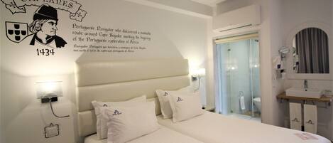 Hotelkamer met twee bedden, een nachtkastje, een aan de muur bevestigd telefoon en een badkamer zichtbaar door een glazen deur.