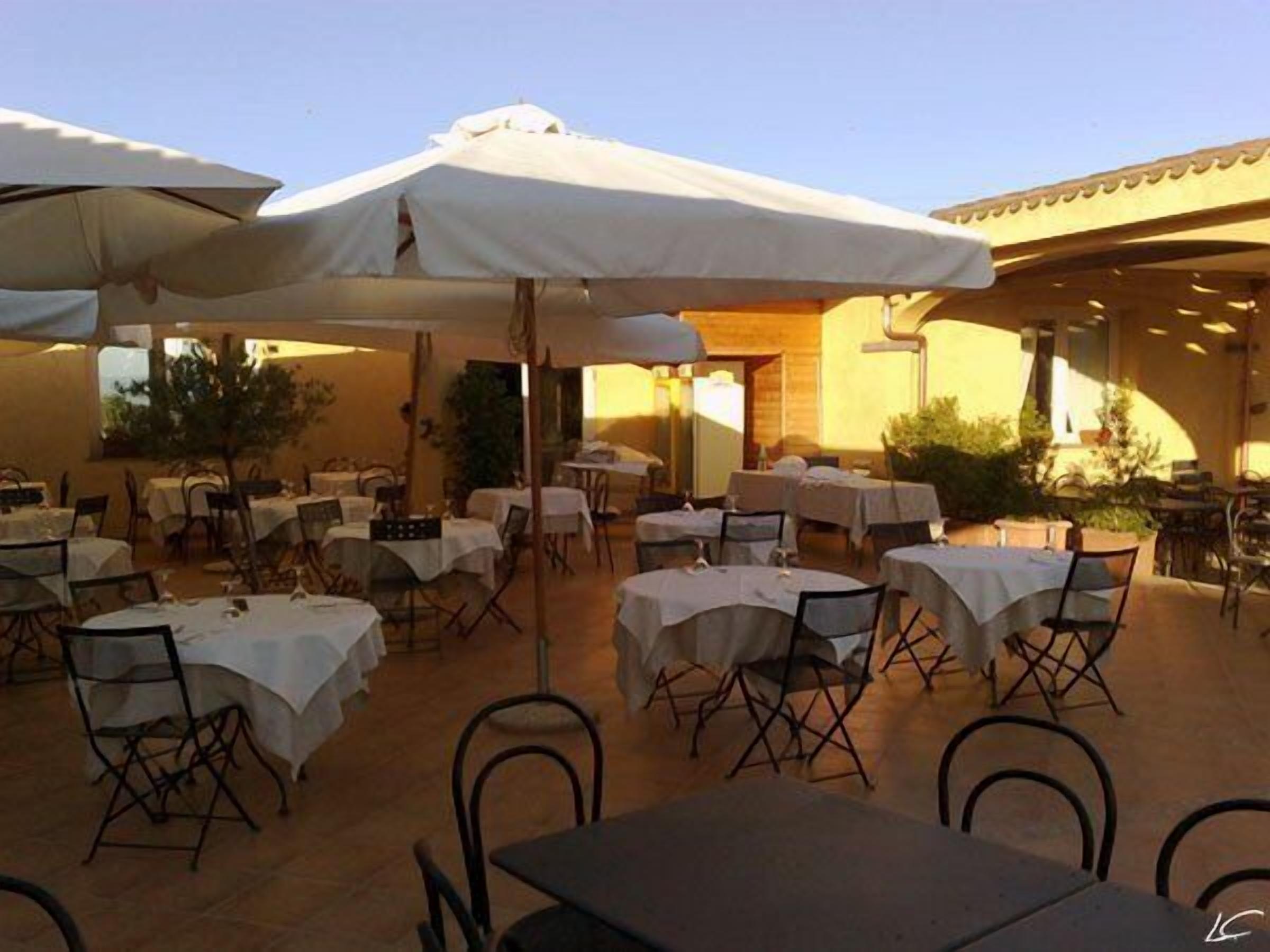 An outdoor dining area with tables and chairs, covered by umbrellas, and a building in the background.