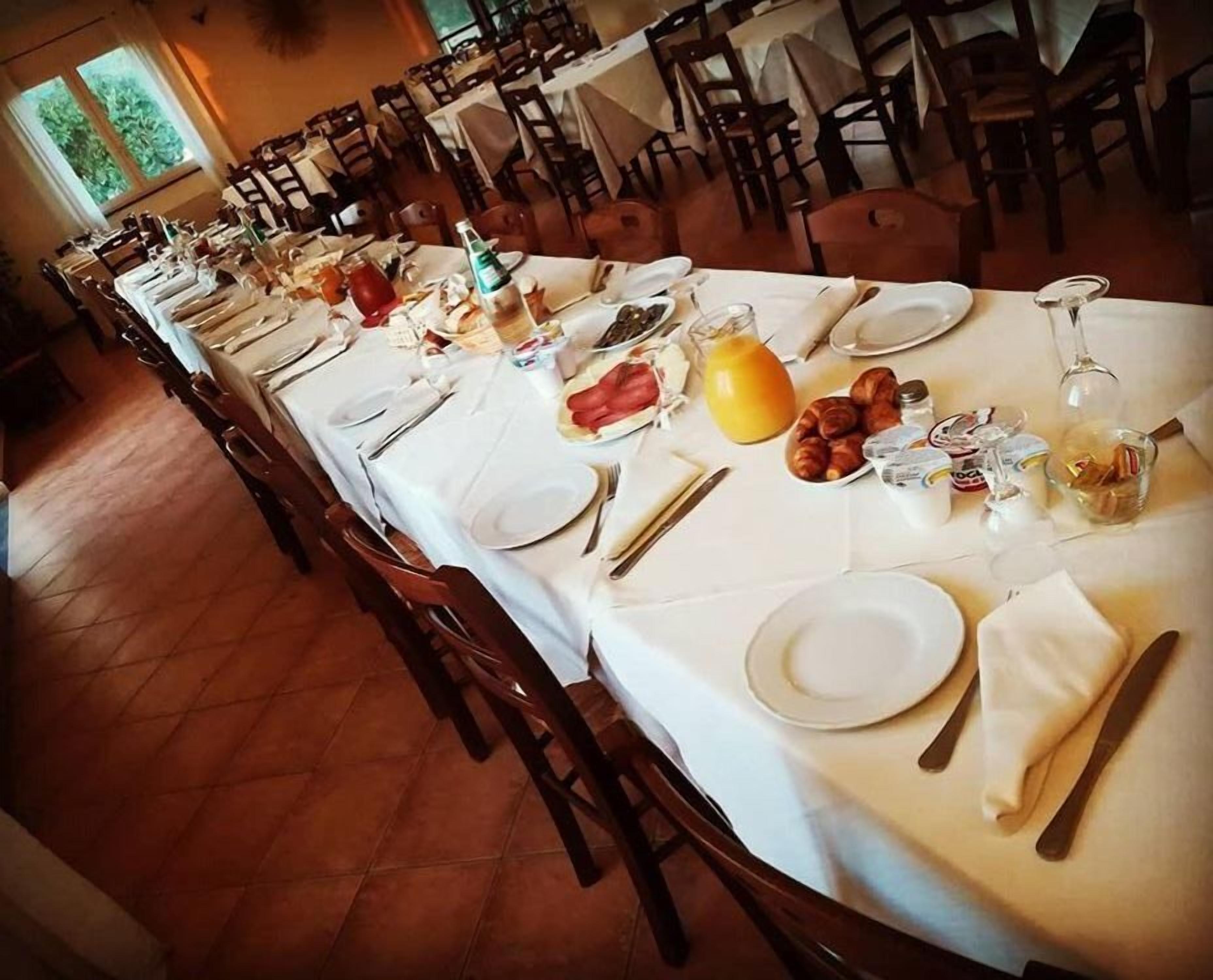 Une longue table à manger dressée dans un restaurant, avec des assiettes, des couverts et des aliments pour le petit-déjeuner.