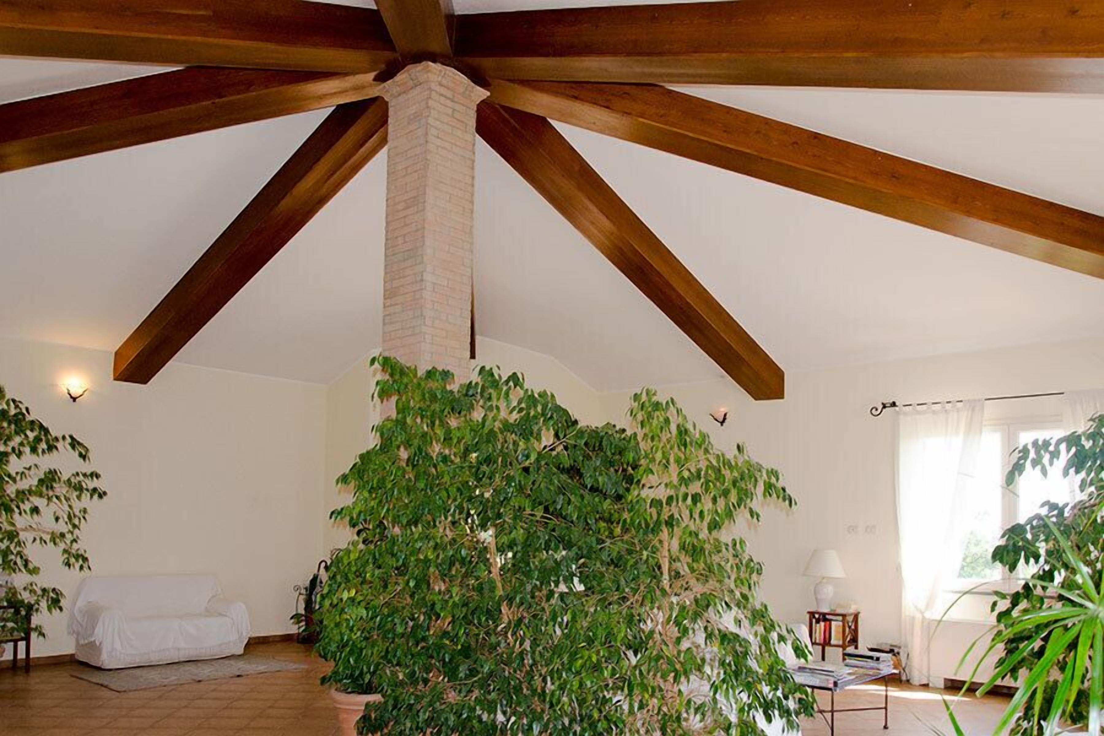 A spacious room with exposed wooden beams, a brick chimney, and a large potted plant.