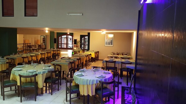 A restaurant with multiple round tables set for dining, featuring a variety of chairs and table settings.