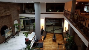 Een ruime lobby met een hoge plafond, een bakstenen muur en een houten vloer. Er is een zithoek met een bank en een bijzettafeltje.