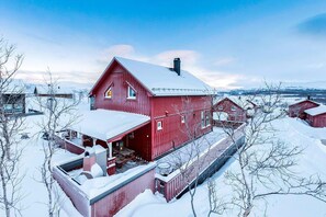 A red wooden house with a snow-covered roof, surrounded by snow-covered trees and a clear sky. - RIBO Apartment Katterjokk (Riksgränsen)