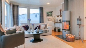 A cozy living room with a fireplace, a sofa, a coffee table, and a view of the outdoors. - RIBO Apartment Katterjokk (Riksgränsen)