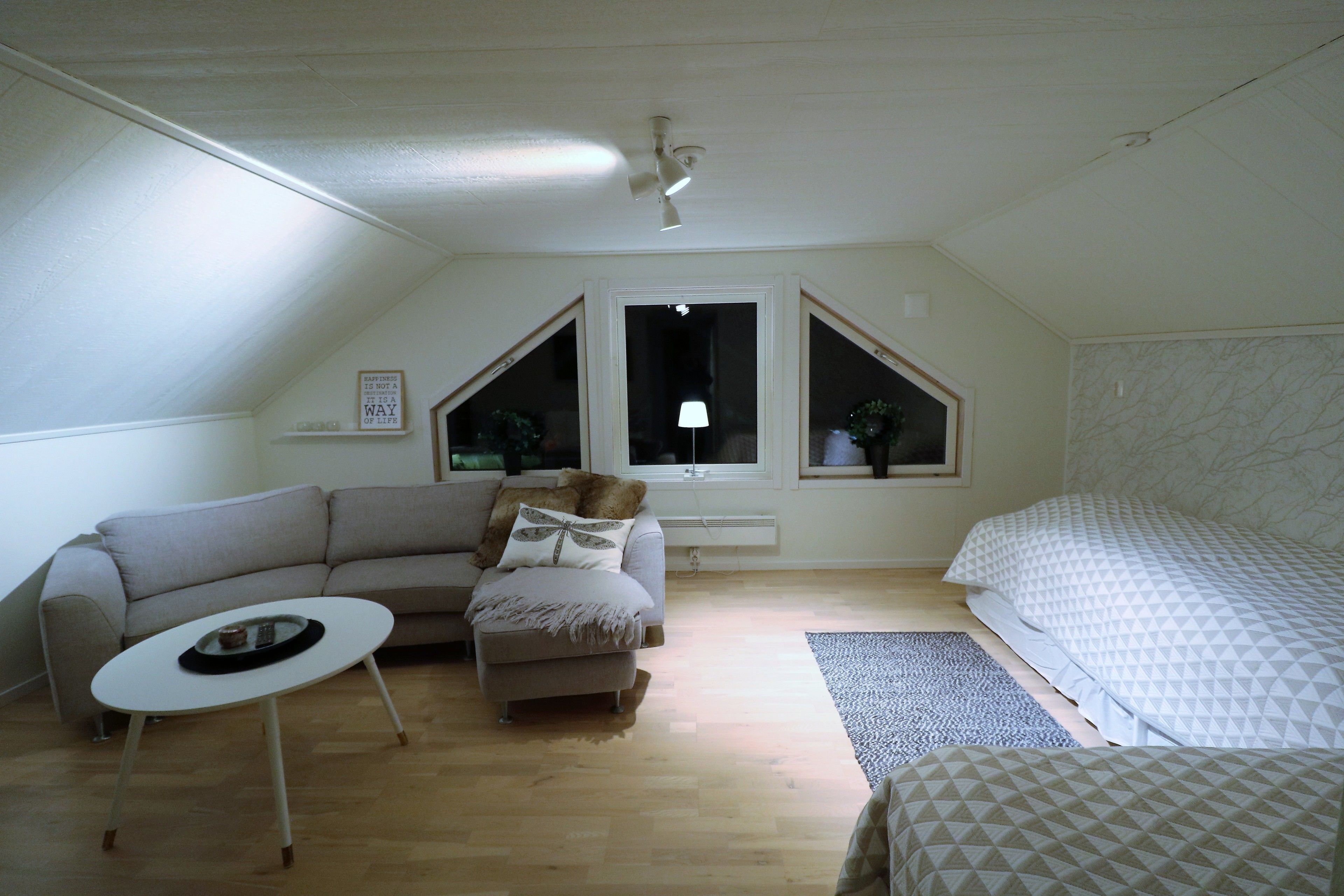 A room with a sloped ceiling, a sofa, a small table, a bed, and a window with a view.