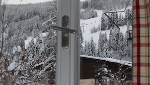 Blick aus dem Fenster auf eine verschneite Landschaft mit Seilbahn, Bäumen und Gebäuden.