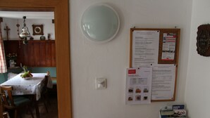 Ein Essbereich mit Tisch für zwei Personen, einer Wandleuchte und einem Korkbrett mit verschiedenen Mitteilungen.