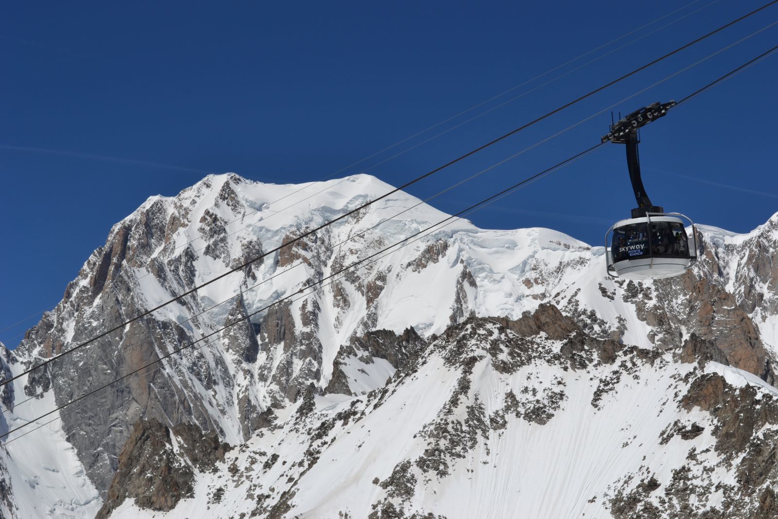 Un teleférico asciende una montaña nevada con afloramientos rocosos.