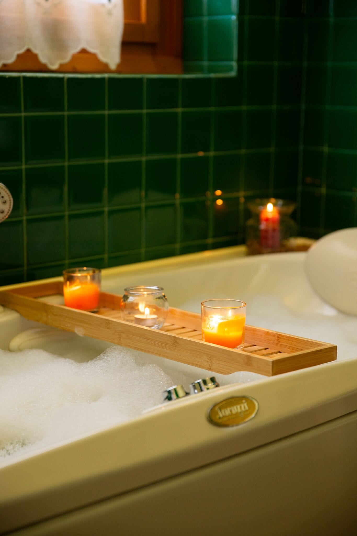 Una bañera con una bandeja de madera que sostiene velas y un vaso de jugo de naranja.