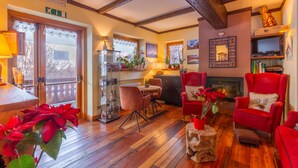 A cozy living room with wooden floors, a fireplace, red armchairs, and a dining area with a table and chairs. - Shatush Hotel (Courmayeur)