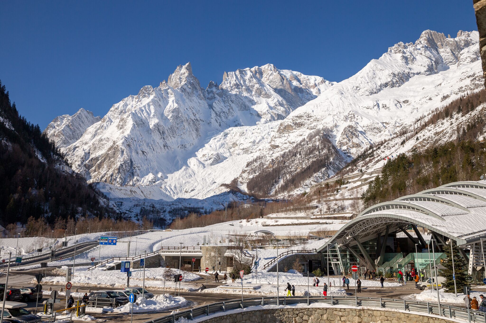Estación de esquí con montañas nevadas, un edificio moderno de fachada de vidrio y un telesilla en primer plano.