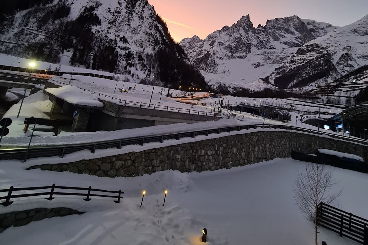 Paisaje nevado de una montaña con un puente de piedra y un aparcamiento.