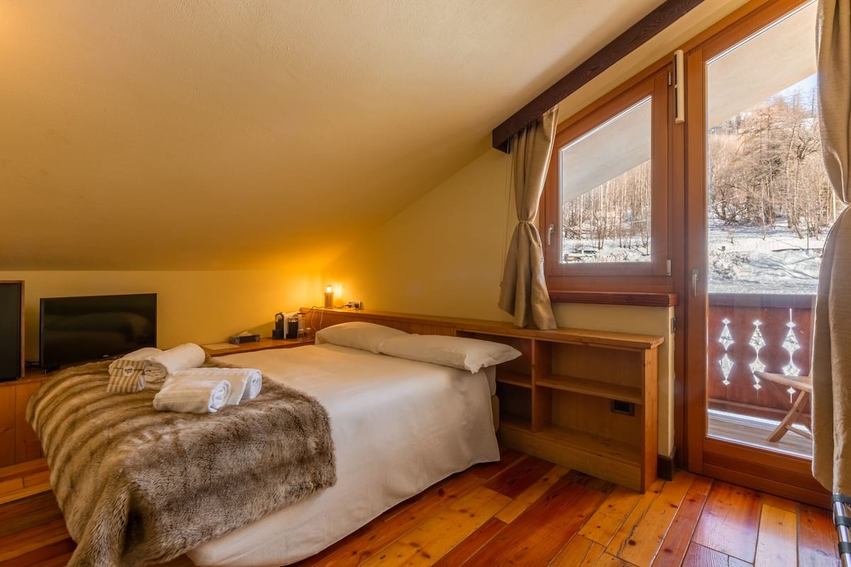 Un dormitorio acogedor con una cama grande, suelo de madera, televisor y ventana con vistas a un paisaje nevado.
