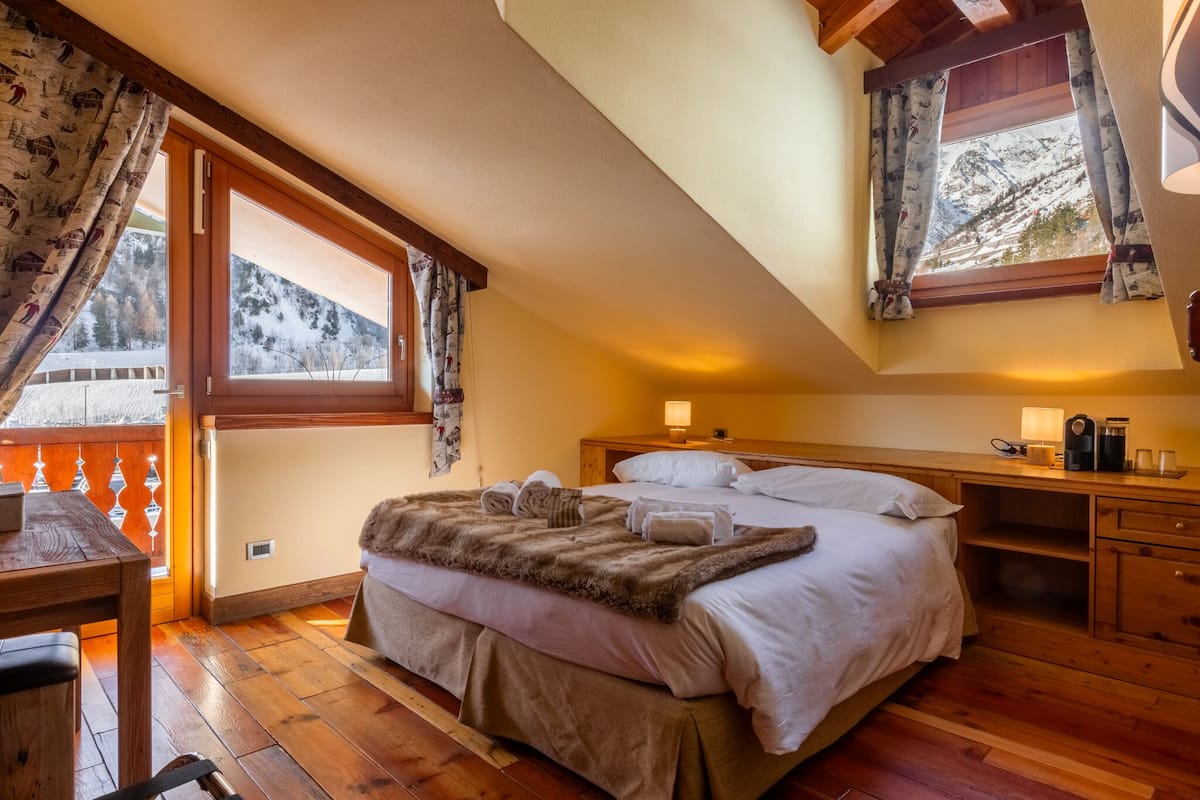 Un dormitorio acogedor con una cama grande, muebles de madera y vistas a montañas nevadas a través de la ventana.
