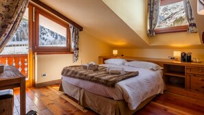 A cozy bedroom with a large bed, wooden furniture, and a view of snowy mountains through the window. - Shatush Hotel (Courmayeur)