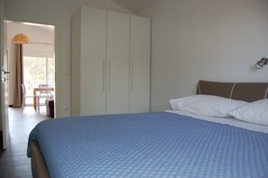 A bedroom with a large bed, a wardrobe, and a view of an outdoor area with a table and chairs.