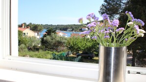 A window with a vase of flowers and a view of houses and trees. - Gorgonia Suites (Sali)