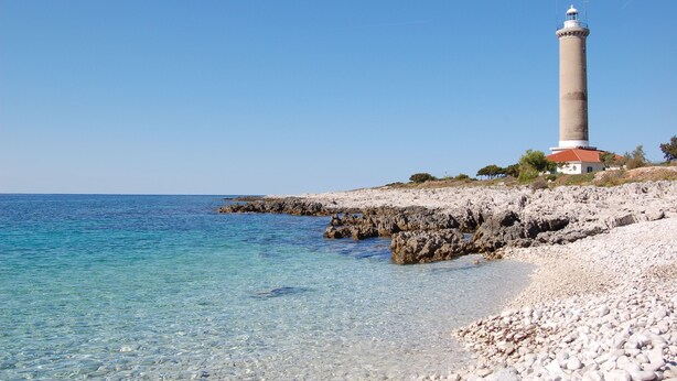 A coastal scene with a lighthouse, clear blue water, and rocky shoreline. - Gorgonia Suites (Sali)