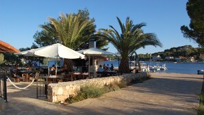 An outdoor dining area with tables and umbrellas, a stone wall, and a view of the water and boats. - Gorgonia Suites (Sali)