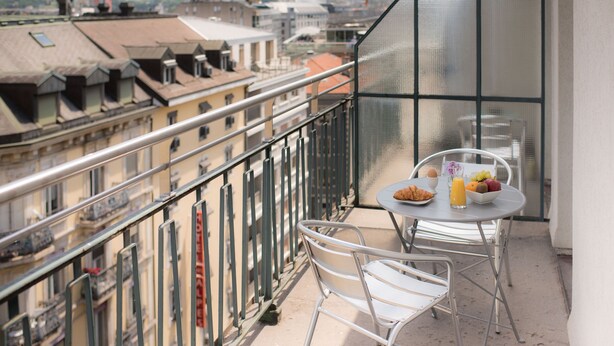 A balcony with a table set for breakfast, overlooking a cityscape with buildings and mountains. - Hotel Montana (Geneva)